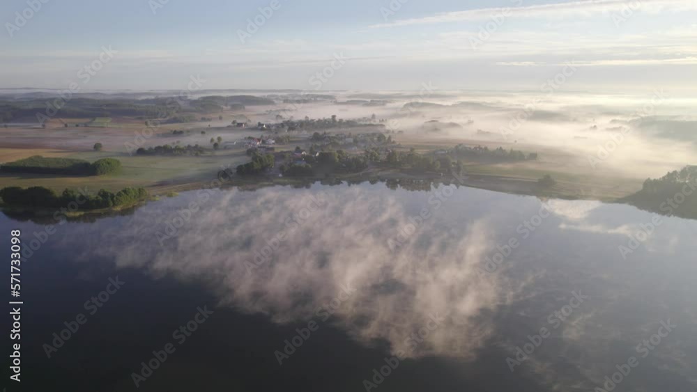 Foggy morning on a beautiful lake surrounded by forests and fields. A small village located near a lake in fog and morning sun. Foggy morning on a beautiful lake surrounded by forests and fields. A small village located near a lake in fog and morning sun.