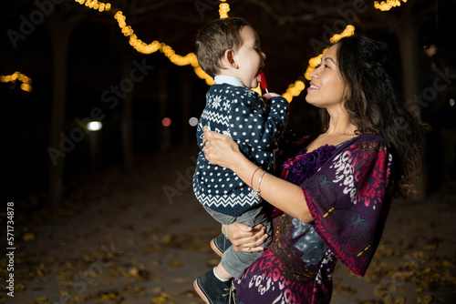 Dark-skinned mother and son playing at night on the street. The woman plays with the child in her arms in a park in autumn. African mother concept.