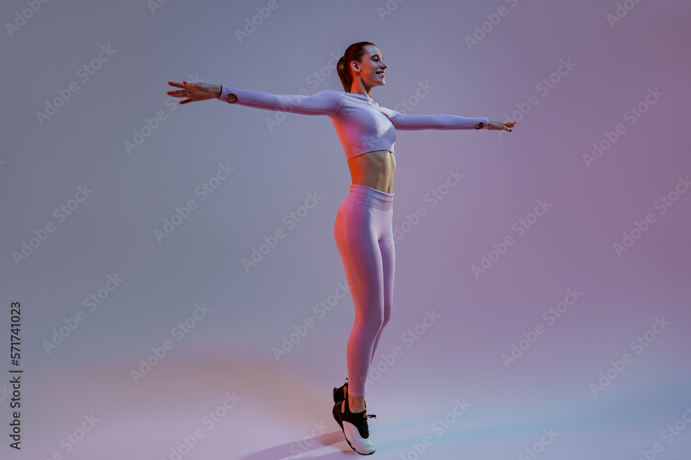 Happy woman wearing sportswear stand with raised up arms on studio background. High quality photo