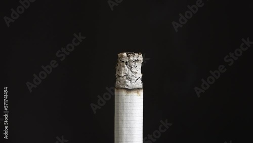 Closeup of a cigarette burning and making smoke and ashes against a black background