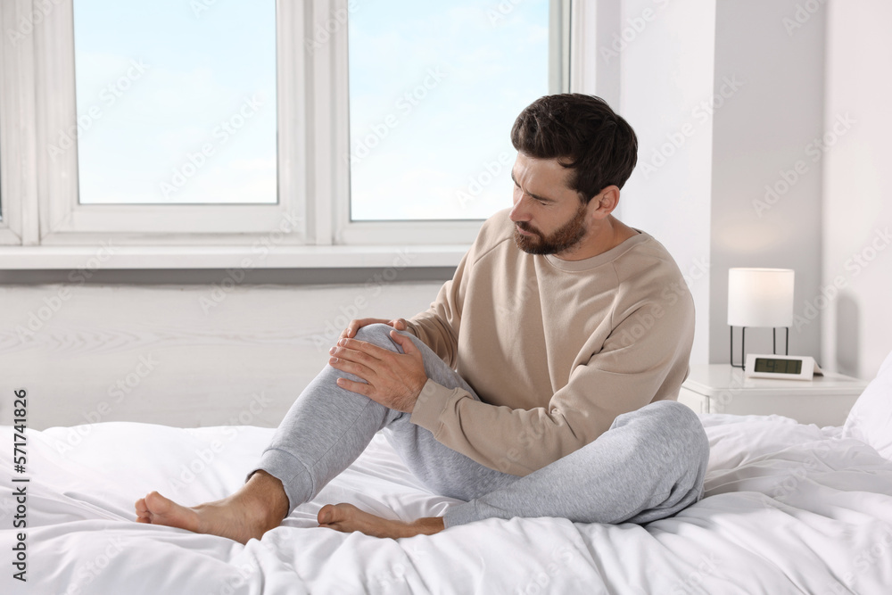 Man suffering from leg pain on bed at home Man suffering from leg pain on bed at home