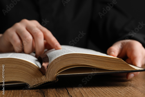 Closeup of woman reading Bible at wooden table, focus on book
