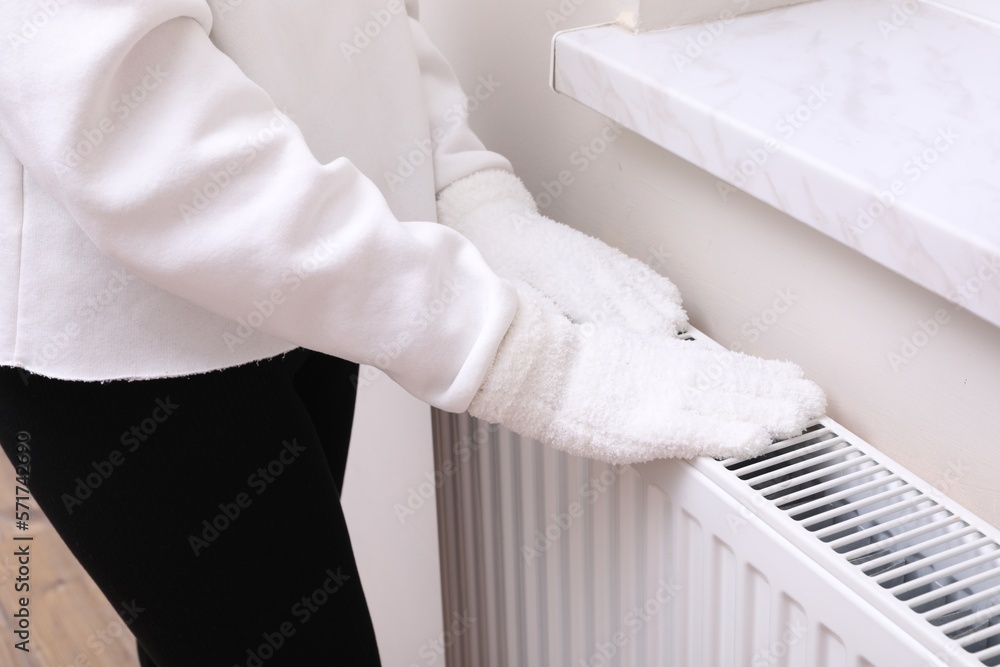 Girl warming hands on heating radiator indoors, closeup Girl warming hands on heating radiator indoors, closeup