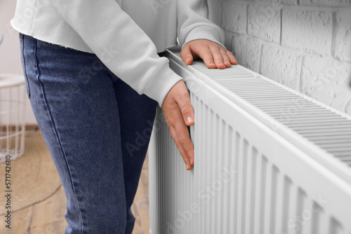 Girl warming hands on heating radiator indoors, closeup