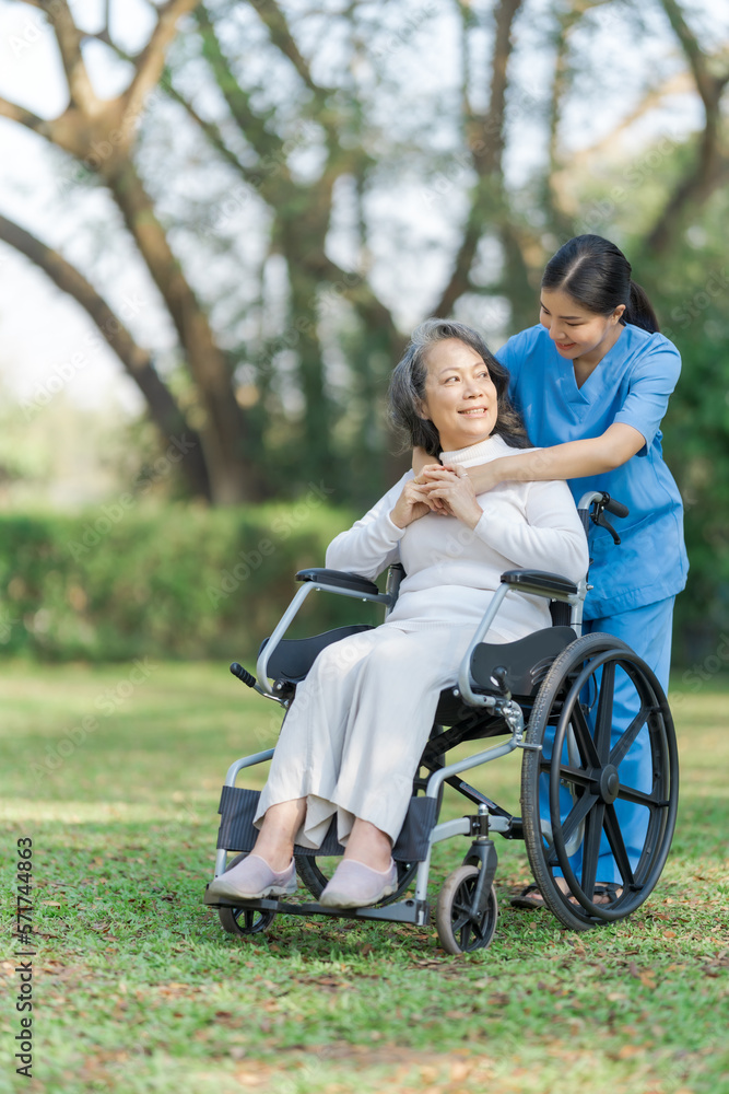 Young asian care helper with asia elderly woman on wheelchair relax together park outdoors to help and encourage and rest your mind with green nature. Hugging Young asian care helper with asia elderly woman on wheelchair relax together park outdoors to help and encourage and rest your mind with green nature. Hugging