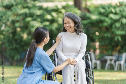 Young asian care helper with asia elderly woman on wheelchair relax together park outdoors to help and encourage and rest your mind with green nature. © NanSan