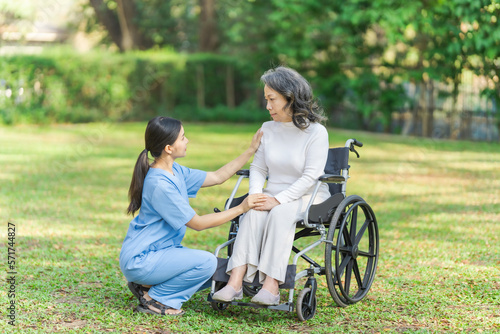 Young asian care helper with asia elderly woman on wheelchair relax together park outdoors to help and encourage and rest your mind with green nature.