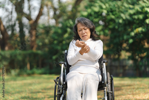 Asian old woman sitting on a wheelchair outdoors in the park Have pain in the arms and wrists