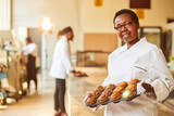 middle aged african chef short hair wearing glasses holding muffins in a industrial kitchen