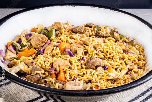 Japanese yakisoba with stir-fried noodles in metallic white pan on table with white tablecloth and black background photo