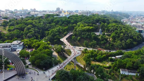 Recently built pedestrian-bicycle bridge over Vladimirsky descent and Peoples' Friendship Arch cinematic landscape. Drone panning to reveal spectacular view of Kyiv, and wide Dnipro river photo