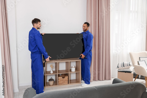 Male movers installing plasma TV near white wall in new house