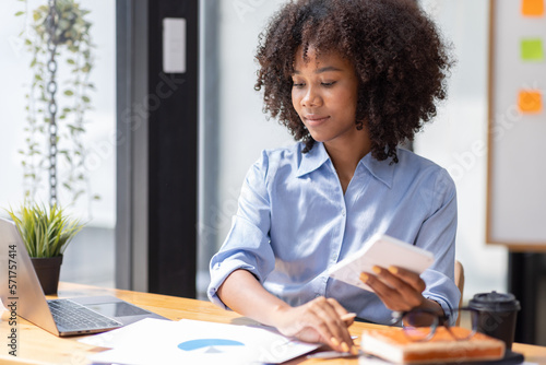 Accountant Young african businesswoman in afro hairstyle Using Calculator For documents Accounting financial sitting at computer in workplace office 