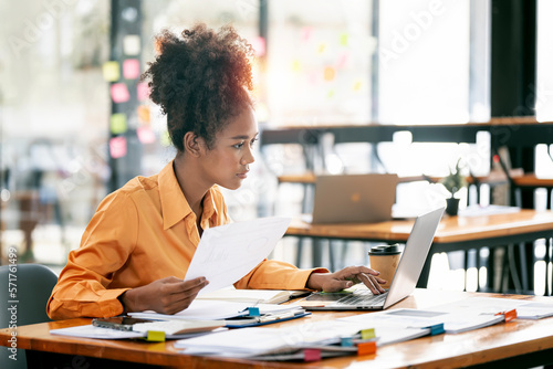 Young ethnic businesswoman looking seriously working on laptop computer and document at her desk office.