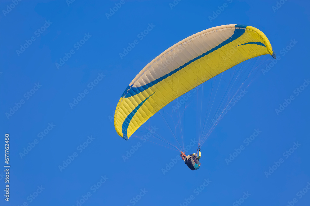 A yellow paraglider gliding across a clear blue sky A yellow paraglider gliding across a clear blue sky