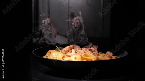 Delicious shrimp ragout with pasta rotating on black plate isolated on dark background