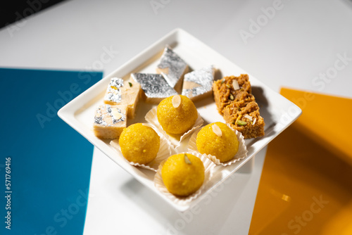 Various Indian desserts are served on a white dish: round 'laddu', square beige 'mawa burfi', square brown 'mohanthal', and diamond 'kaju'. photo