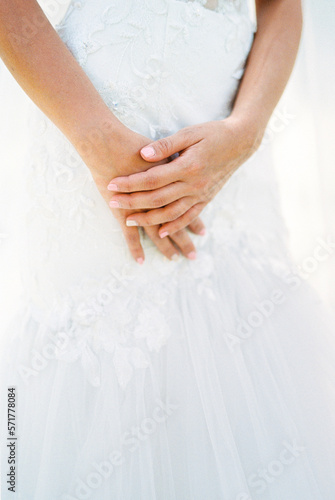 Bride folded her hands on the hem of her wedding dress. Close-up