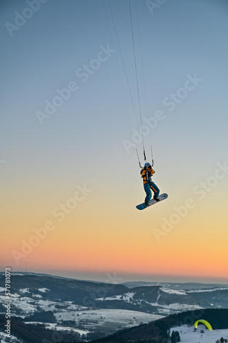 Snowkiting, snowboarder flies with a towing kite through the sunset in the sky of the Wasserkuppe in the Rhoen, Hesse, Germany