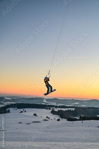 Snowkiting, Snowboarder fliegt mit Zugdrachen durch den Sonnenuntergang am Himmel der Wasserkuppe in der Rhön, Hessen, Deutschland
