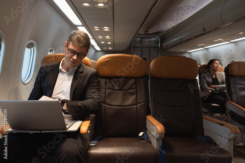 Businessman working on laptop while sitting in airplane cabin. Business work and travel concept. © boonsom