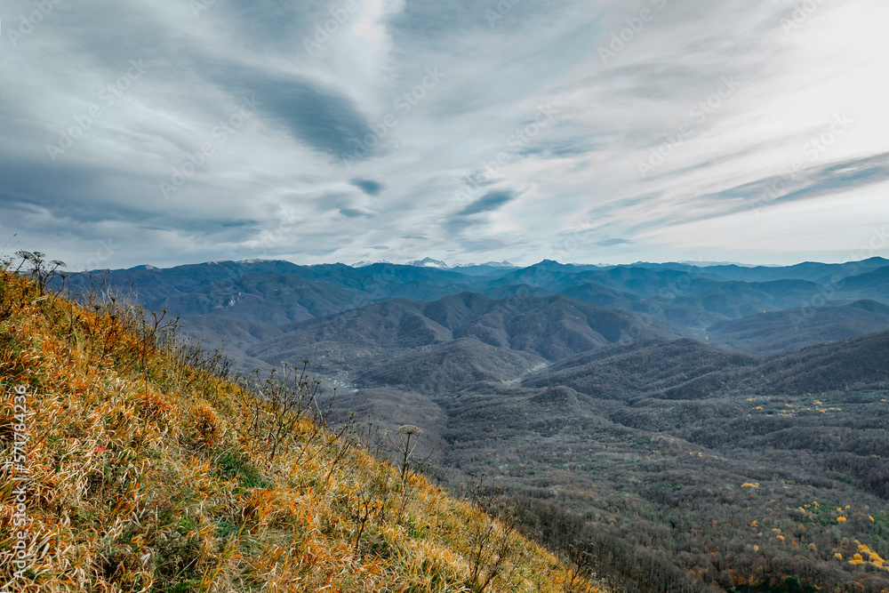 View of the mountain range under a cloudy sky. Panoramic view of the Caucasus mountains. Mountain landscape with beautiful Caucasian nature. Landscape of a mountain range on an autumn morning.