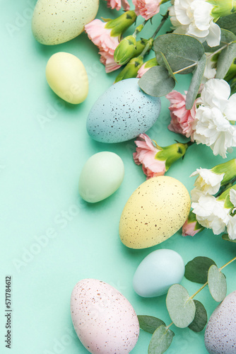 Easter colored eggs and a bouquet of white and pink carnations with eucalyptus branches on a soft green background.