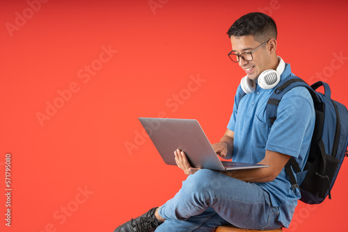Happy young college man with glasses and white headphones on his neck, sitting using his laptop