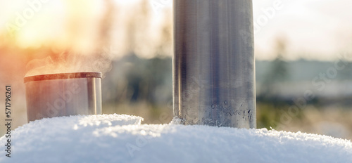 Metal thermos with a hot drink on the background of a winter mountain waterfall. Insulated drink container in the snow