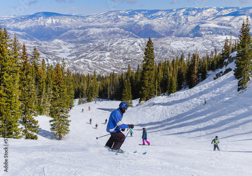 Senior male downhill skier skiing in Colorado ski resort on nice winter afternoon; forest and mountains in background