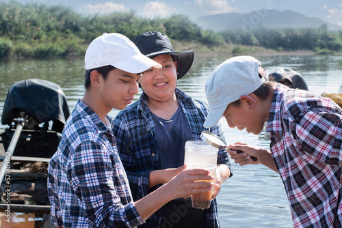 Asian boys holding magnifying glass and transparent plastic tubes to to the experiment of water from local river to study the fertility of the river and environmental problems around their villages.