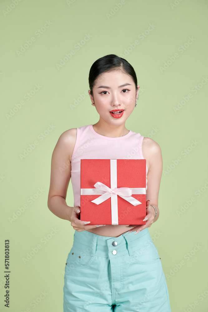 Happy pretty young woman holding gift box over green background Happy pretty young woman holding gift box over green background