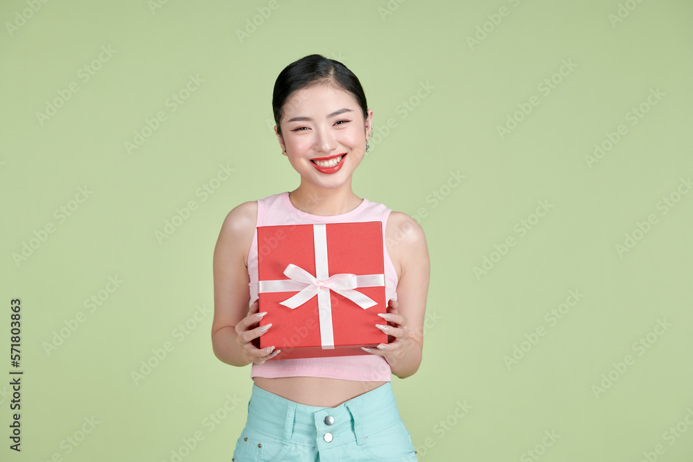 Portrait of a happy pretty asian woman holding present box while standing isolated over green pastel background Portrait of a happy pretty asian woman holding present box while standing isolated over green pastel background