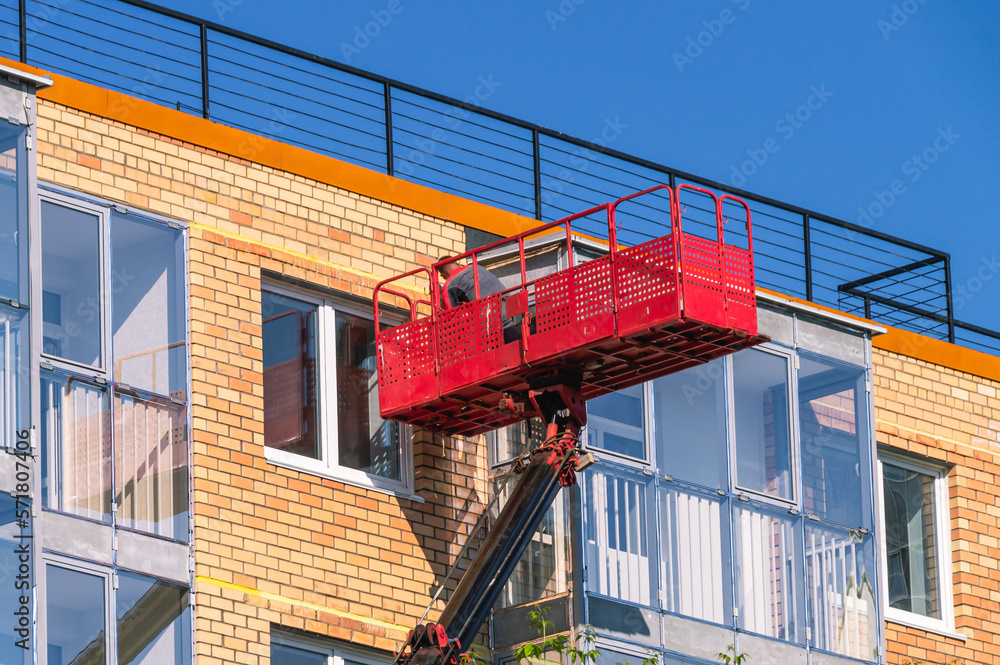 Construction lift for finishing works at height. A construction worker works in a cradle of a lifting mechanism at a height. High-rise works during the construction of a residential building.