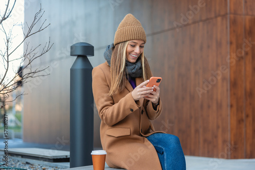 Photography Image of beautiful stylish woman sitting on street bench with legs crossed on su