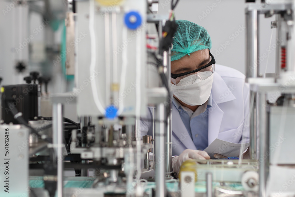 Worker in personal protective equipment or PPE inspecting quality of mask and medical face mask production line in factory, manufacturing industry and factory concept. Worker in personal protective equipment or PPE inspecting quality of mask and medical face mask production line in factory, manufacturing industry and factory concept.