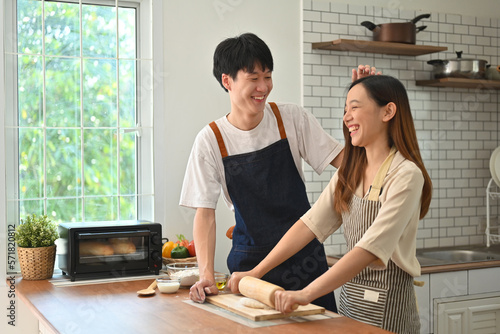 Lovely young asian couple wearing aprons preparing homemade pastry, enjoying leisure time together at home