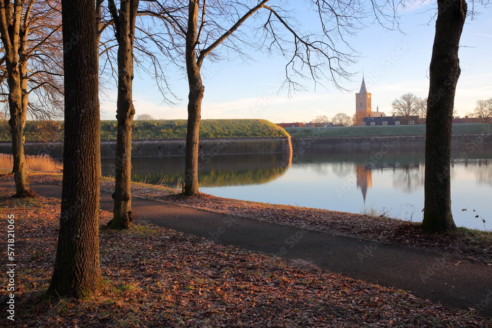 The fortifications and moats of the city of Naarden, Netherlands, with the Grote Kerk church in the background. Picture taken after sunrise in winter in the woods surrounding Naarden