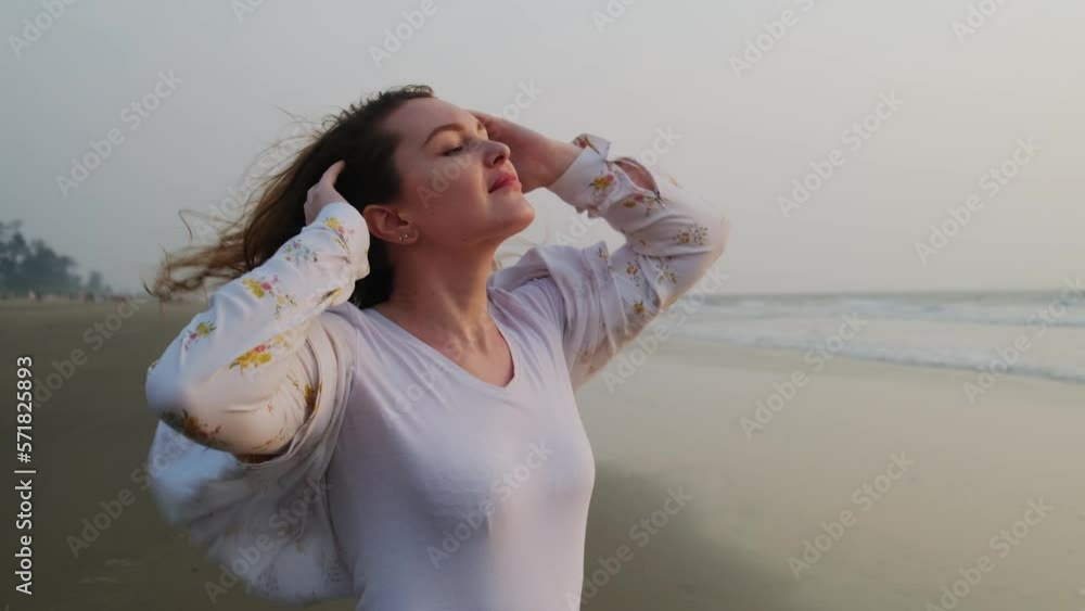 Beautiful young woman with long hair flowing on the wind. Happy female traveller enjoys freedom on the seashore at sunset. Beautiful young woman with long hair flowing on the wind. Happy female traveller enjoys freedom on the seashore at sunset.