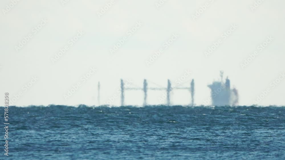 Mirage of cargo ship in the sea beyond the horizon. Ship sailing in the sea. Small waves on the golden surface of warm water with bokeh lights from the sun. Sea, nature and outdoor travel. Mirage of cargo ship in the sea beyond the horizon. Ship sailing in the sea. Small waves on the golden surface of warm water with bokeh lights from the sun. Sea, nature and outdoor travel.