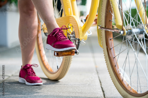 A woman's foot steps on the pedal of her yellow bike in preparation to ride