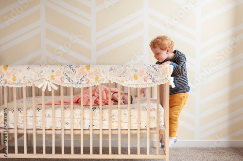 Toddler reaching in crib trying to touch newborn baby's head