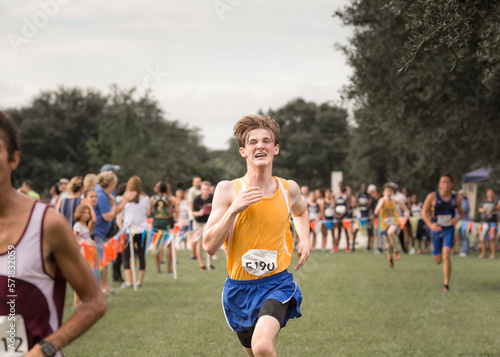 Teen male cross country runner with braces crosses finish line in race