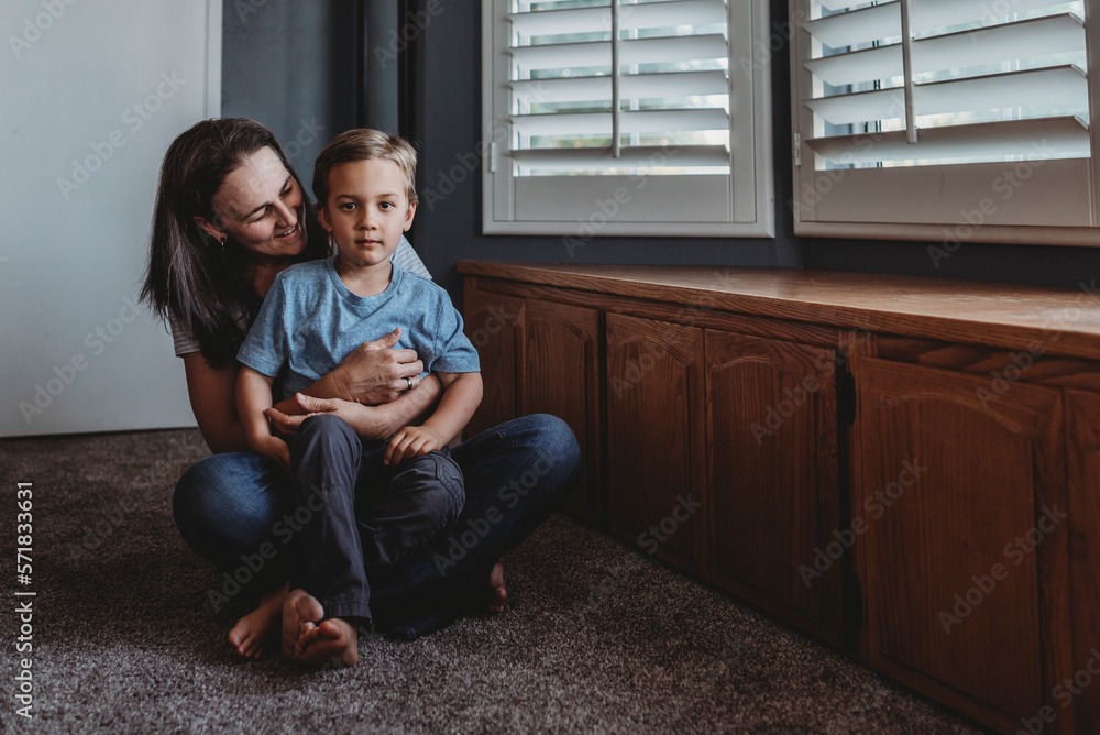 Smiling mom sitting on floor with 5 yr old son on lap near window Smiling mom sitting on floor with 5 yr old son on lap near window