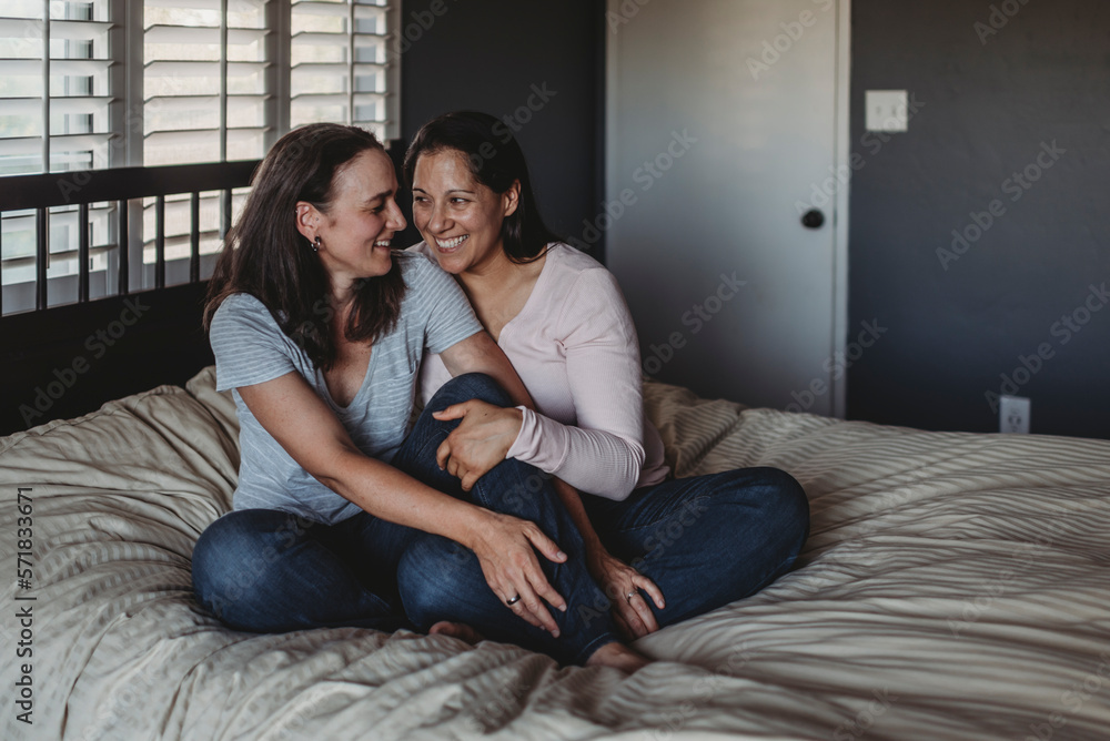 Happy same sex couple sitting on bed laughing together Happy same sex couple sitting on bed laughing together