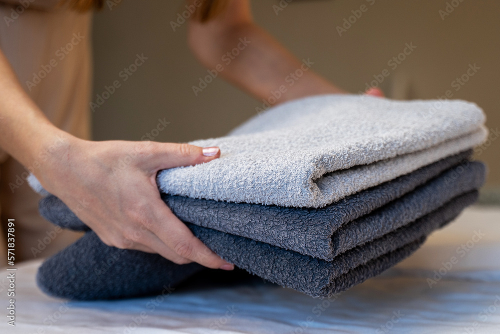 Close-up of hands putting a stack of fresh bath towels on a sheet. Room service maid cleaning the hotel room Close-up of hands putting a stack of fresh bath towels on a sheet. Room service maid cleaning the hotel room