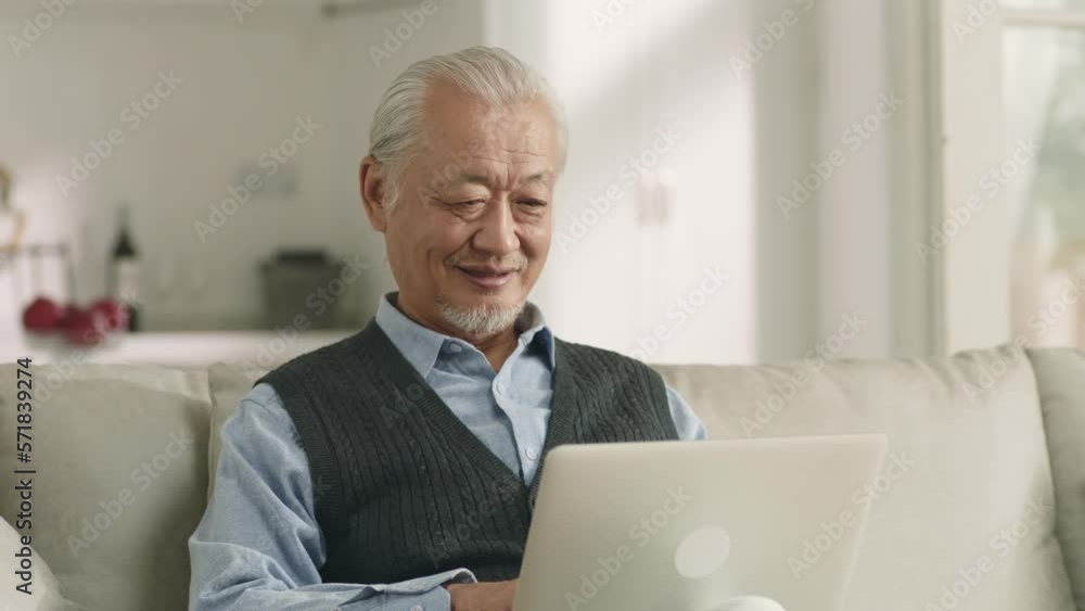 senior asian man sitting on couch at home using laptop computer