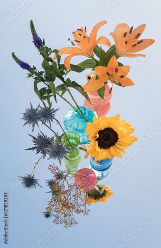 fine art decoration of colorful flowers in glass vases on mirror reflecting the blue sky