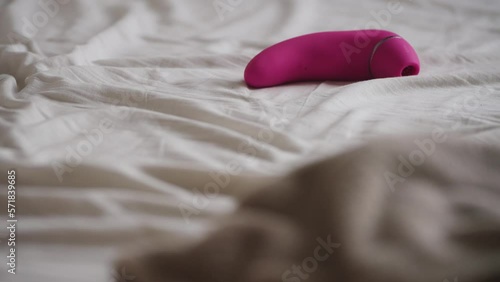 Rack focus from grey sheets to pink vibrator on bed sheets. Handheld.