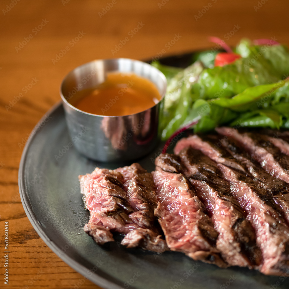 Juicy medium rare meat steak. Meat is cut into pieces and served on plate with sauce and lettuce leaves. Wooden table. Close-up. Soft focus. Juicy medium rare meat steak. Meat is cut into pieces and served on plate with sauce and lettuce leaves. Wooden table. Close-up. Soft focus.